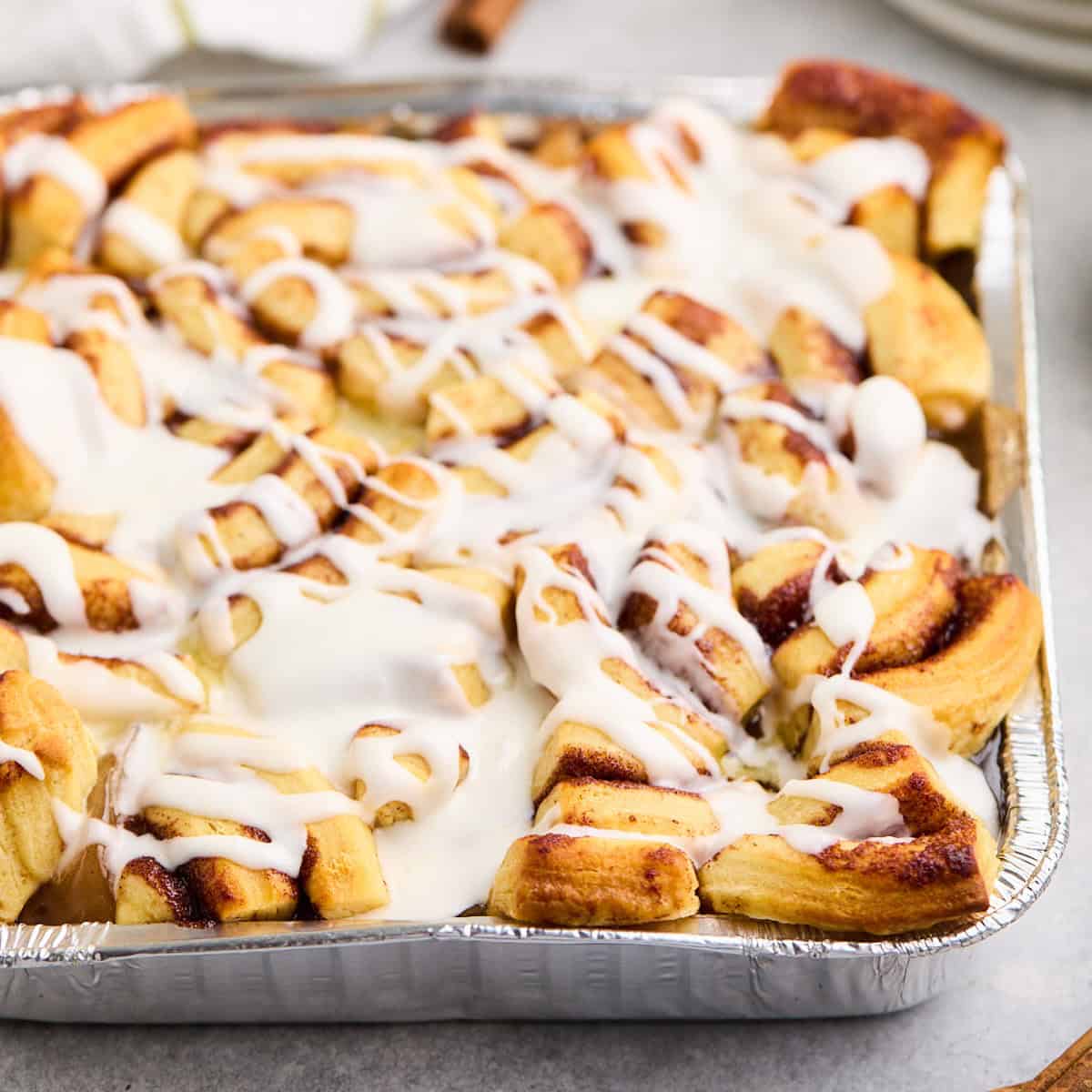 Close-up of a freshly baked cinnamon roll apple cobbler drizzled with icing in a foil baking dish.