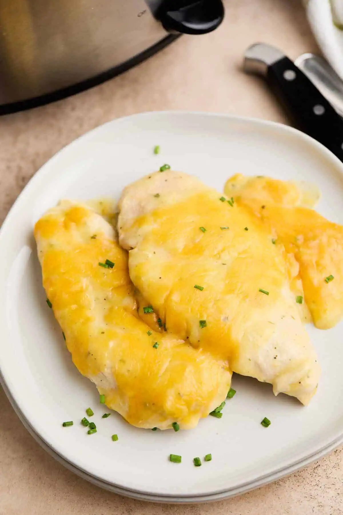 Top-down view of crockpot ranch chicken, showcasing the melted cheddar cheese and fresh chives on top.