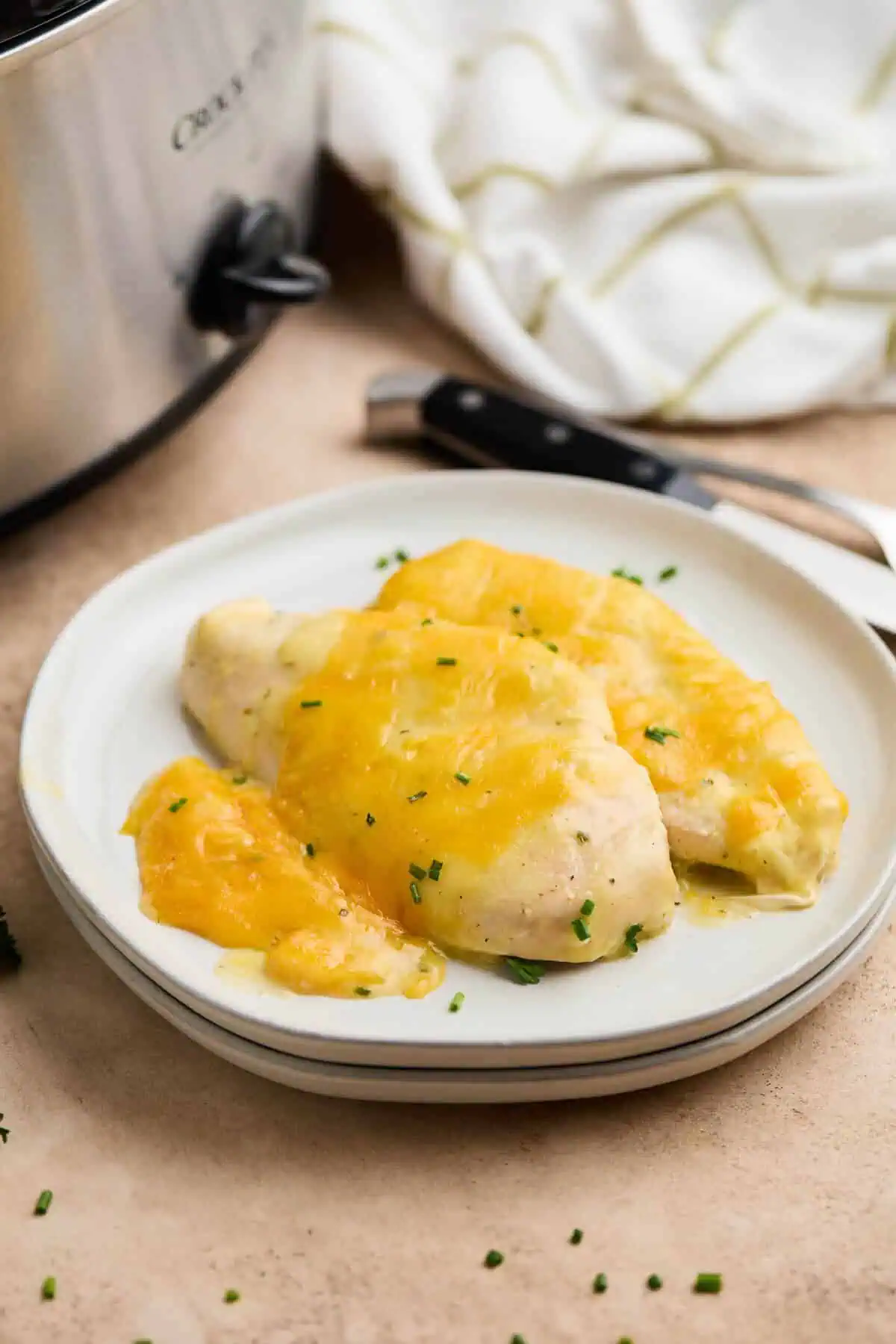 Two servings of crockpot ranch chicken on a white plate, topped with melted cheddar cheese and garnished with fresh chives.