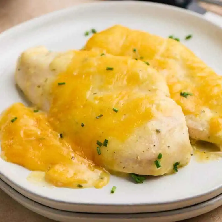 Close-up of a plate with tender chicken breasts covered in melted cheddar cheese, served fresh from the crockpot.