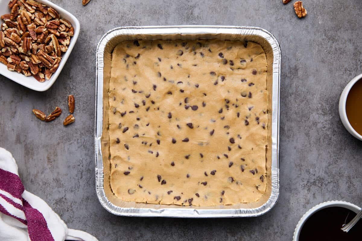 Raw chocolate chip cookie dough pressed into an 8x8-inch pan.