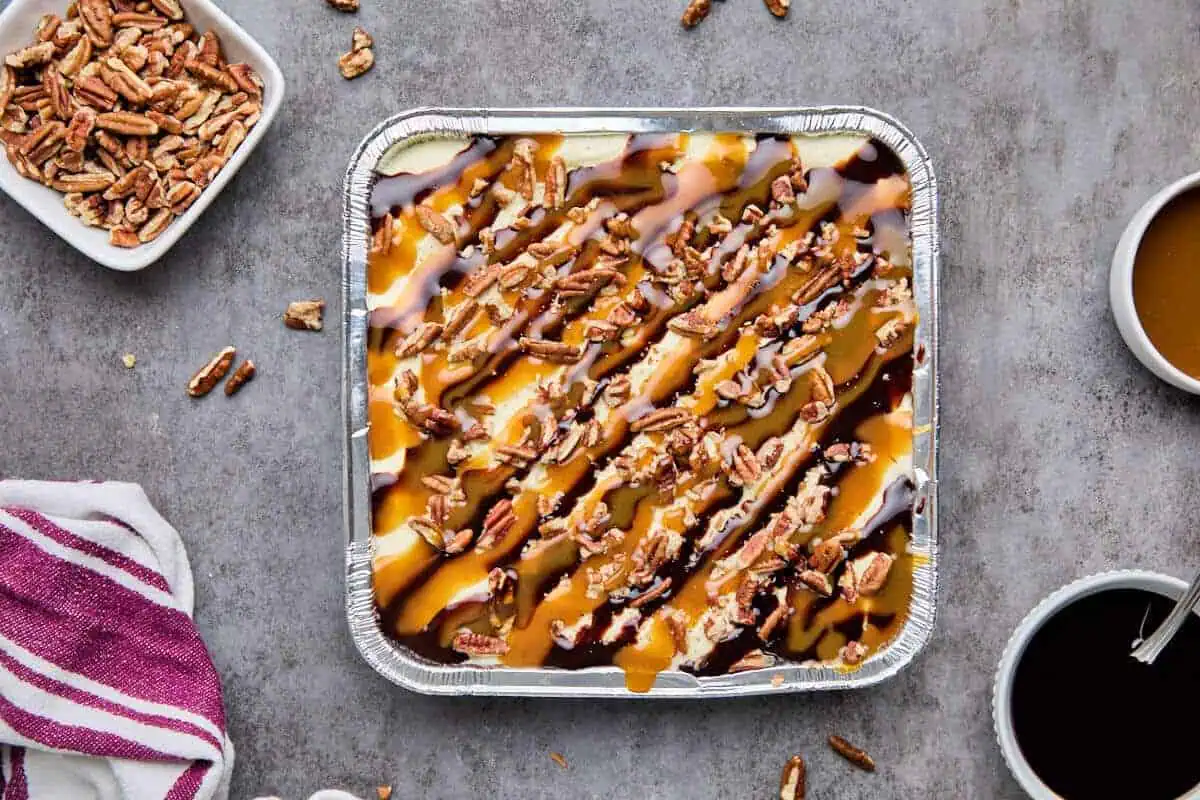 Turtle cheesecake with caramel and chocolate sauce drizzled over chopped pecans, ready to serve.