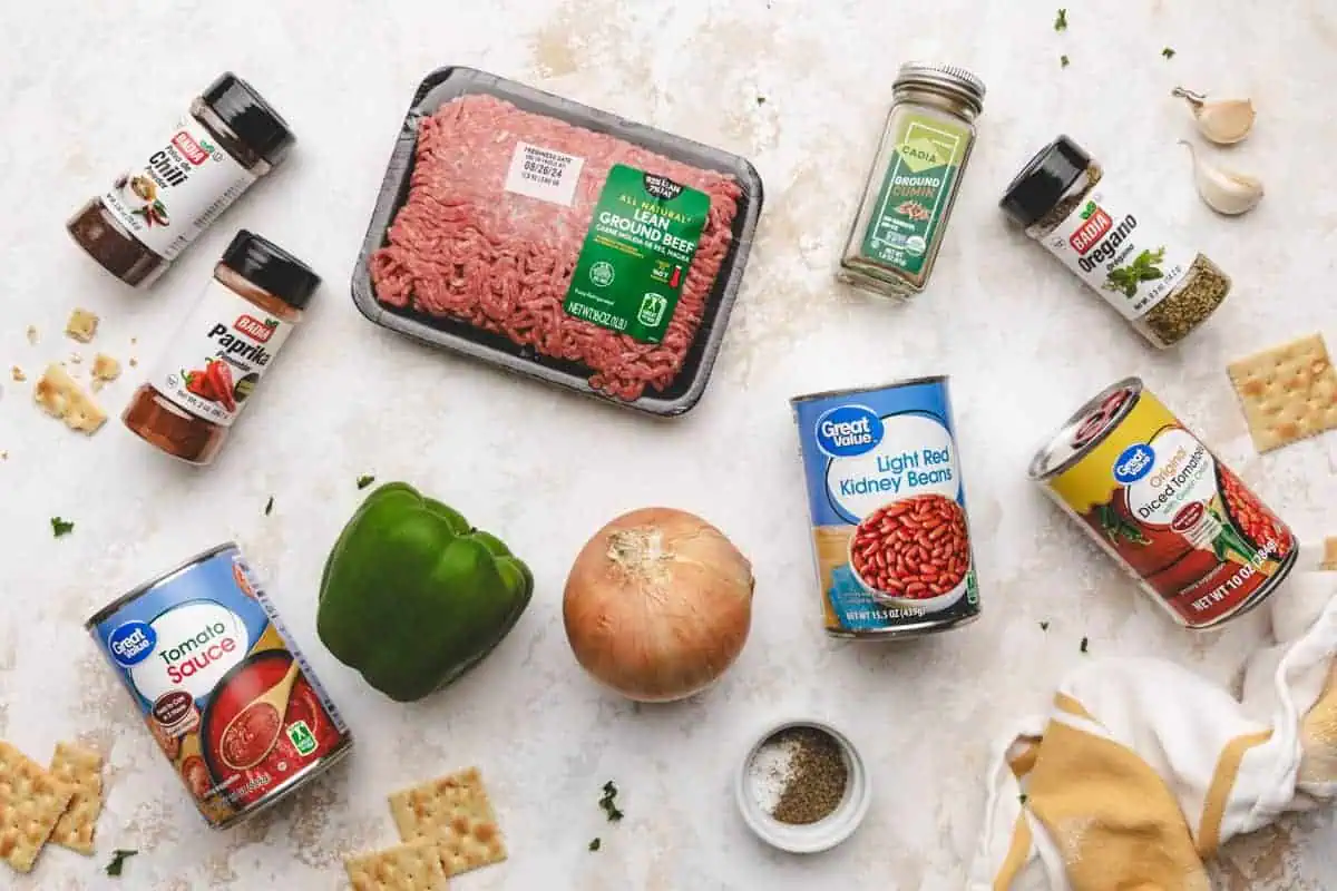 Ingredients laid out for an easy chili recipe, including ground beef, kidney beans, diced tomatoes, green bell pepper, onion, and a variety of spices like chili powder, cumin, and smoked paprika.