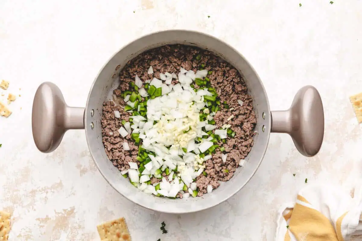 A pot of sautéed onions and green bell peppers added to browned ground beef.