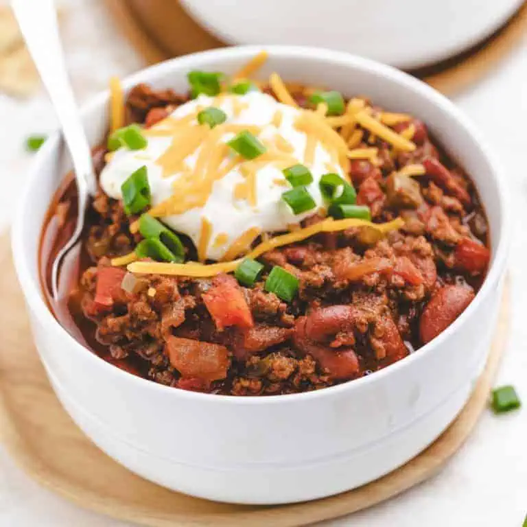 A bowl of the best chili recipe topped with cheddar cheese, sour cream, and green onions.