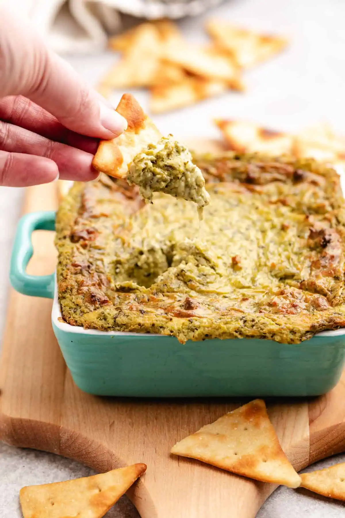 Hand scooping dip from a baking dish.