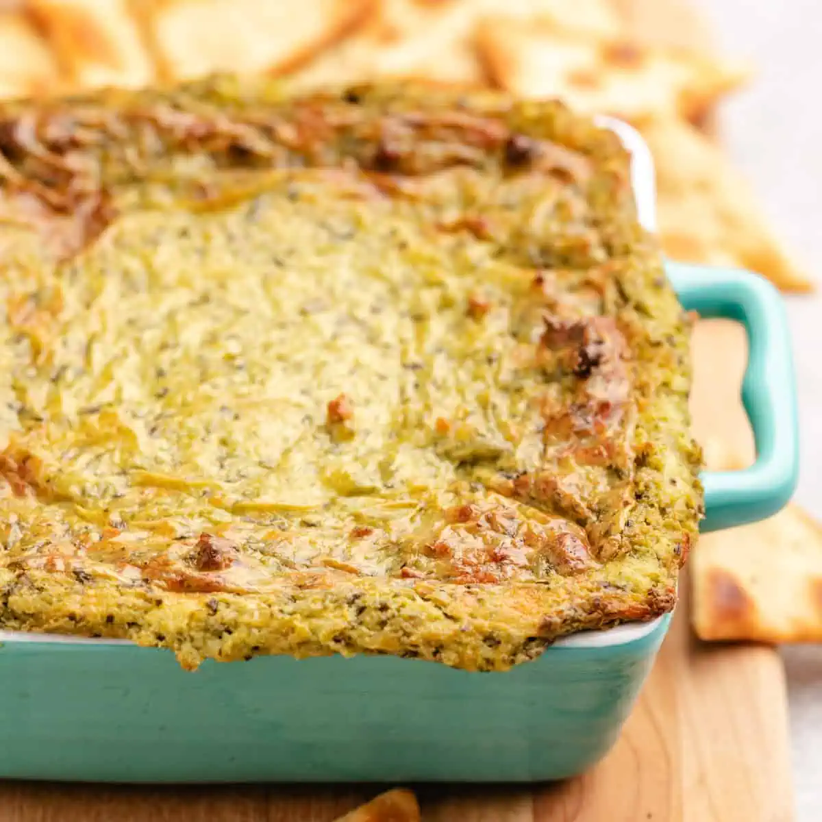 Side view of creamy pesto dip in a teal dish.