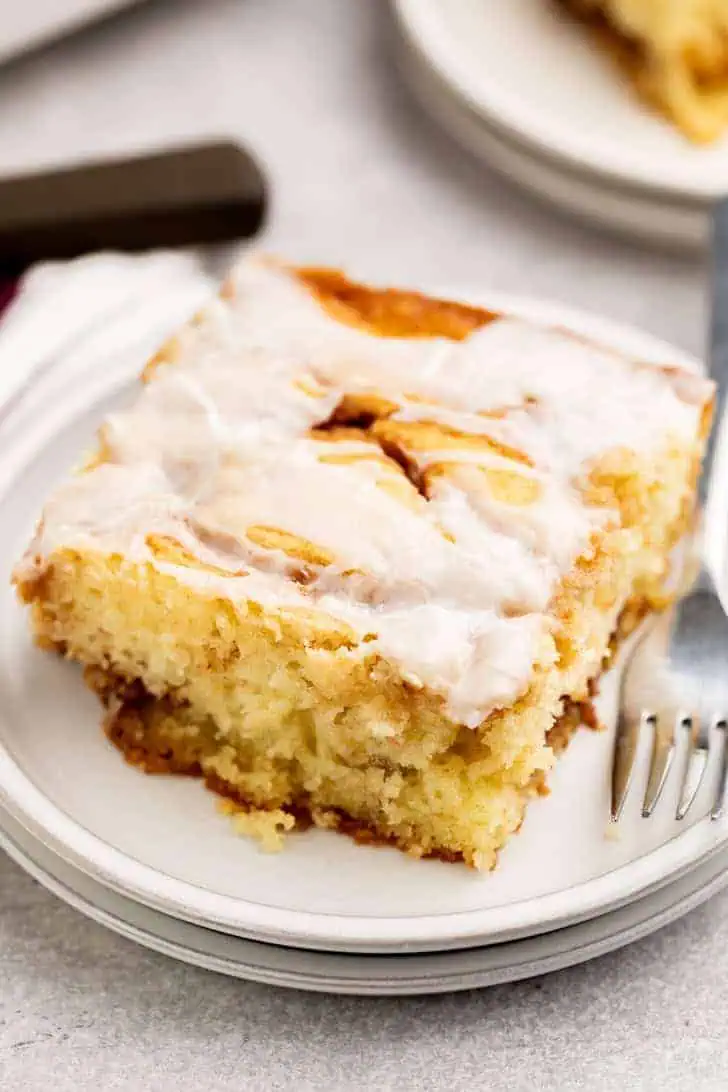 Slice of cinnamon cake with glaze on a stack of plates.