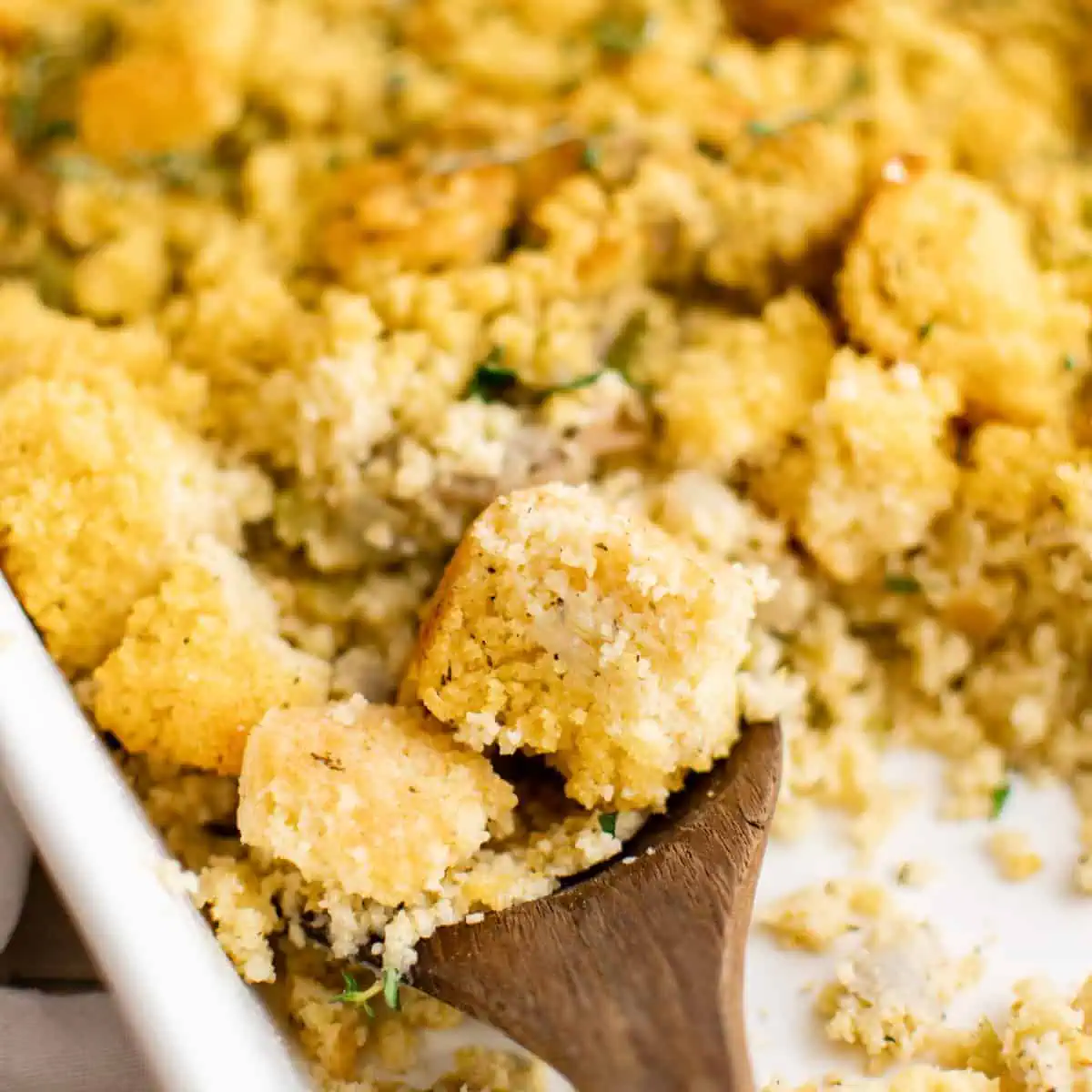 Close up view of a wooden spoon scooping cornbread dressing from a pan.