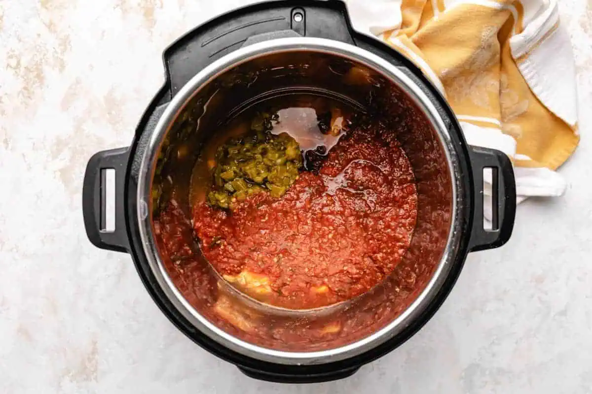 Chicken breasts, salsa, chipotles, seasonings, and chiles in an instant pot.