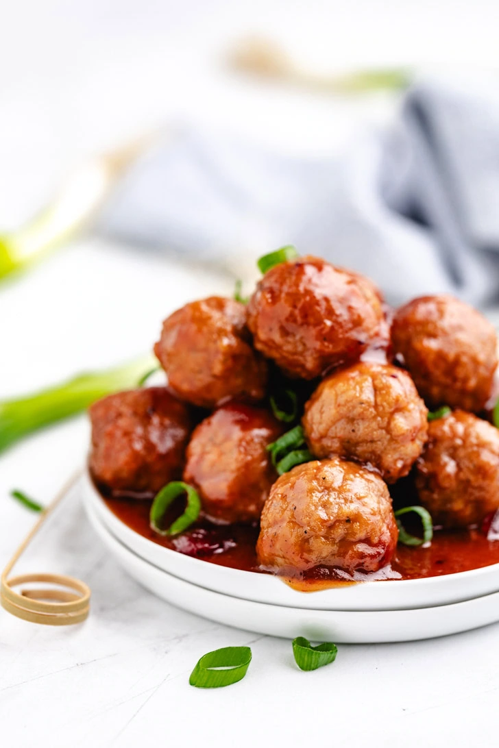 Plate filled with bbq meatballs topped with green onions.