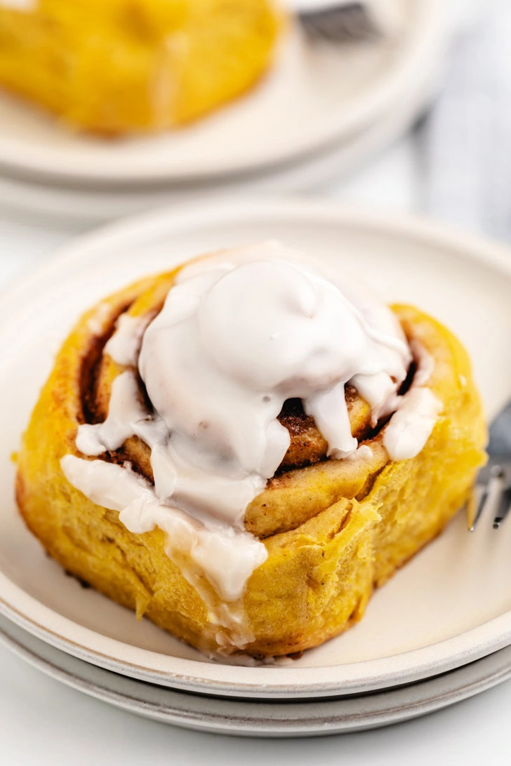 Gooey pumpkin spice cinnamon roll on a stack of plates.