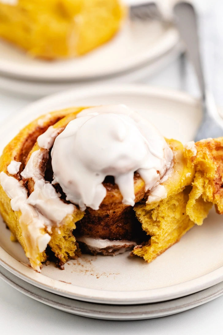 Cinnamon roll torn apart on a stack of off white plates.