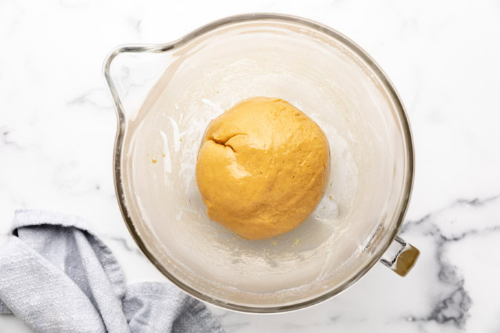 Pumpkin cinnamon roll dough in a glass bowl.