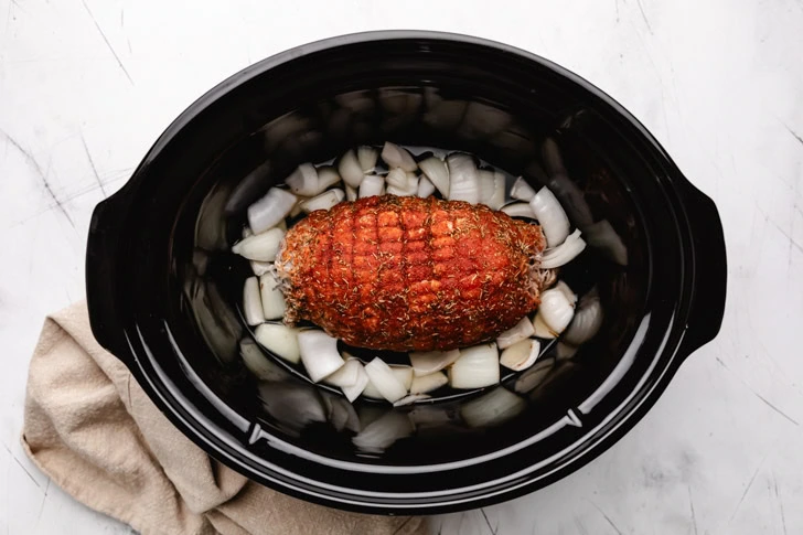 Seasoned turkey over onions in a crock pot.