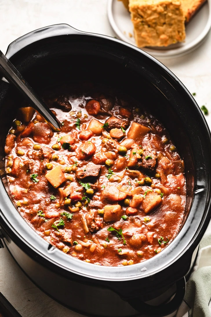 Side view of slow cooker beef stew with a ladle.