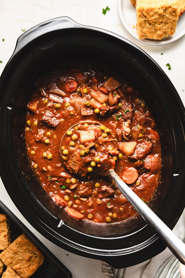 Ladle scooping beef stew from a crock pot.