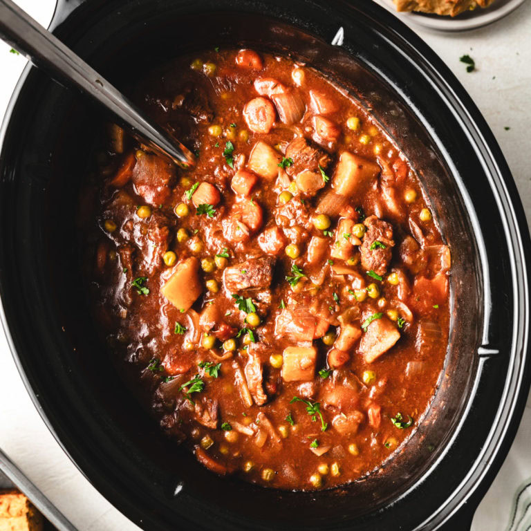 Overhead view of a metal ladle in a slow cooker filled with beef stew.