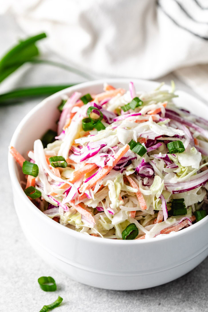 A white bowl filled with fresh coleslaw made from shredded cabbage, carrots, and purple onions.