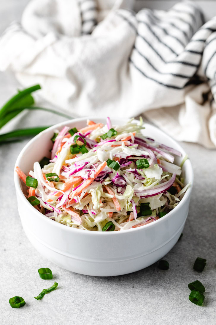 A white bowl filled with homemade coleslaw, garnished with chopped green onions.