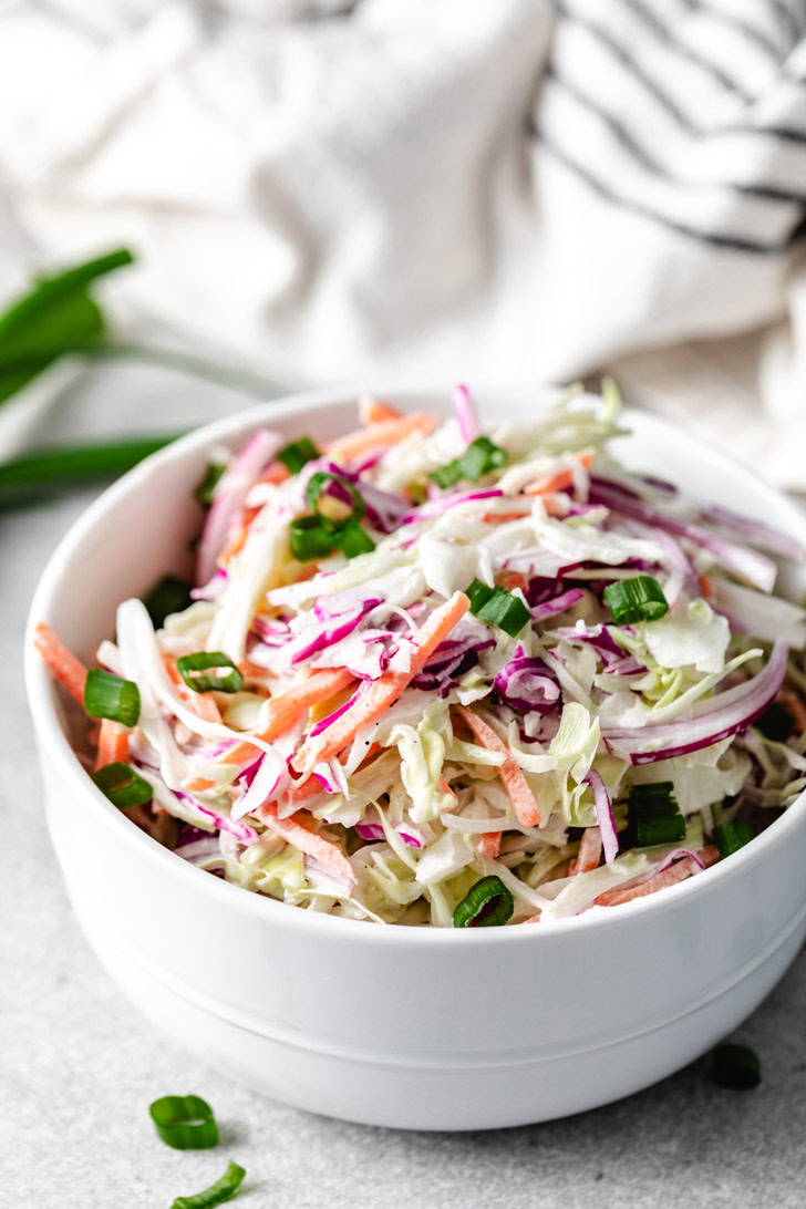 A vibrant coleslaw salad with purple cabbage, carrots, and onions in a white bowl.