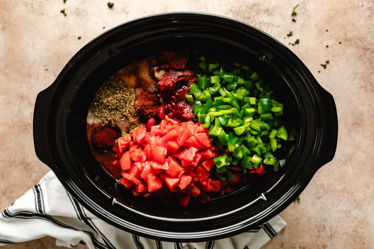 A slow cooker filled with fresh chili ingredients, including diced tomatoes, beans, and peppers.