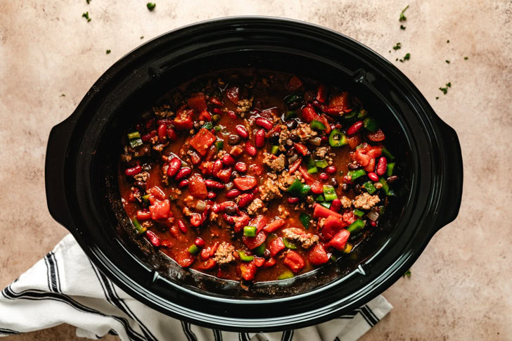 A slow cooker filled with chili after stirring.