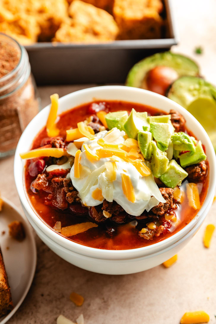 A bowl of chili topped with sour cream, cheese, and diced avocado.