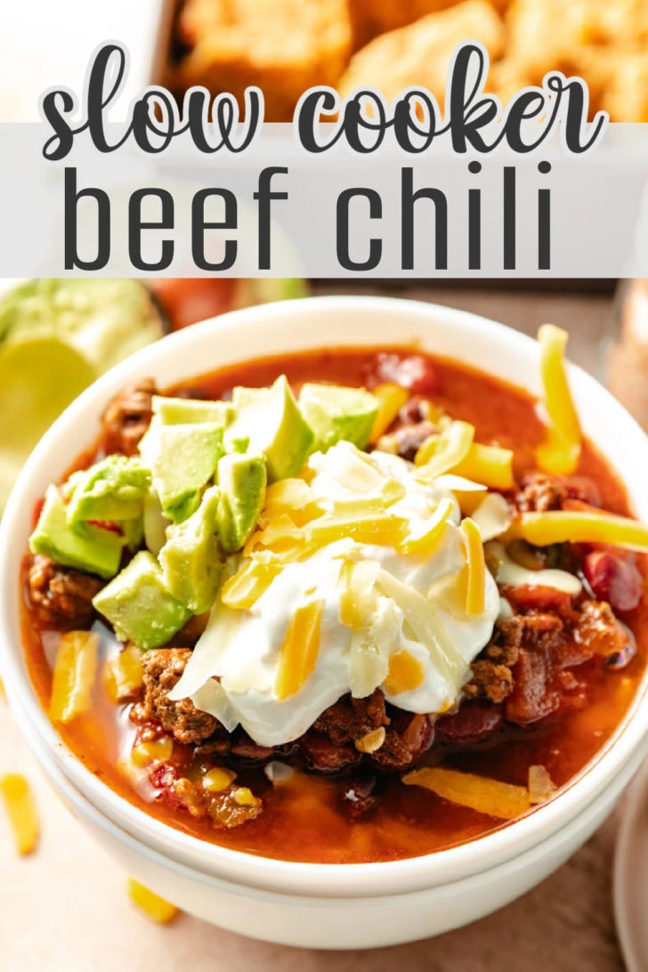 A bowl of beef chili topped with sour cream, cheese, and avocado.