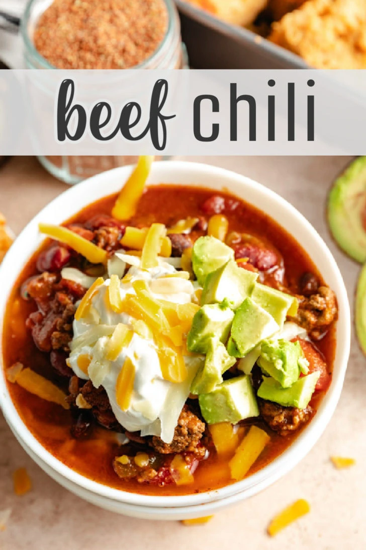 A bowl of beef chili with sour cream, avocado, and shredded cheese on top.