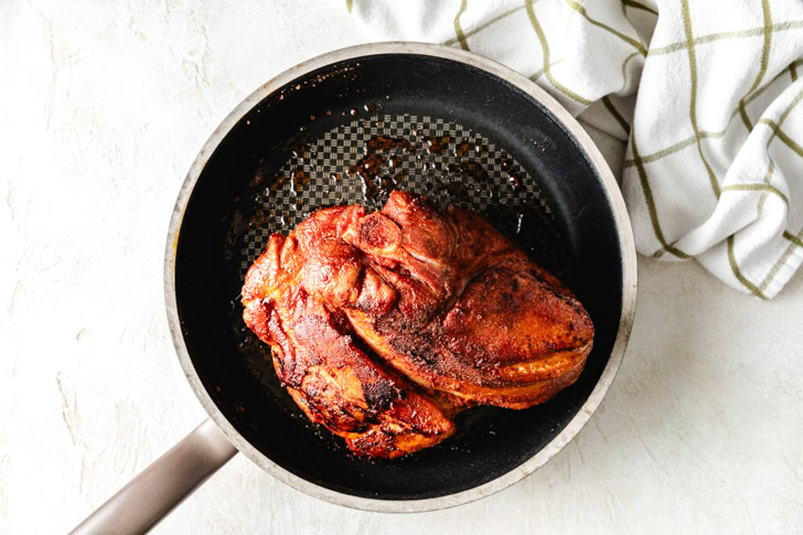 A seared pork shoulder in a skillet.