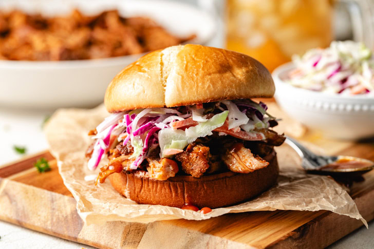 A bbq pulled pork sandwich with sauce and coleslaw on a wooden board.