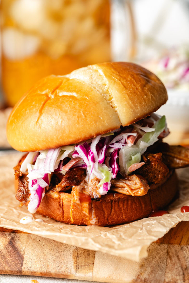 A bbq pulled pork sandwich with sauce dripping onto parchment paper.