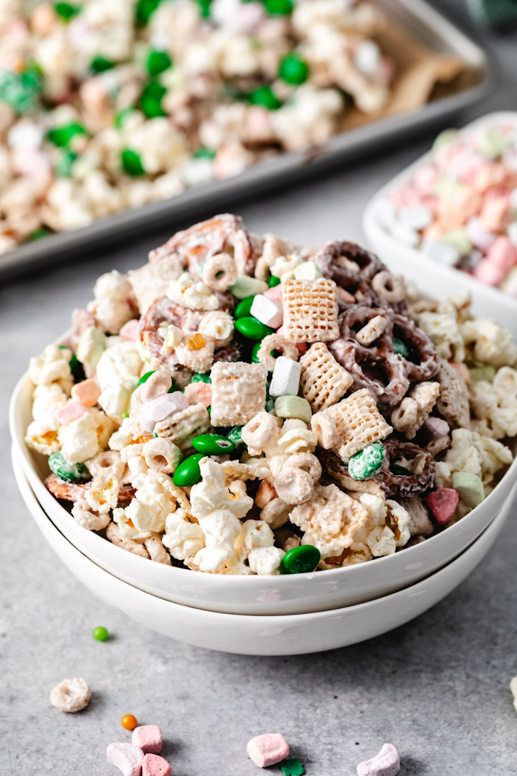 A bowl of snack mix with green m&ms, popcorn, and pretzels coated in vanilla melting wafers.