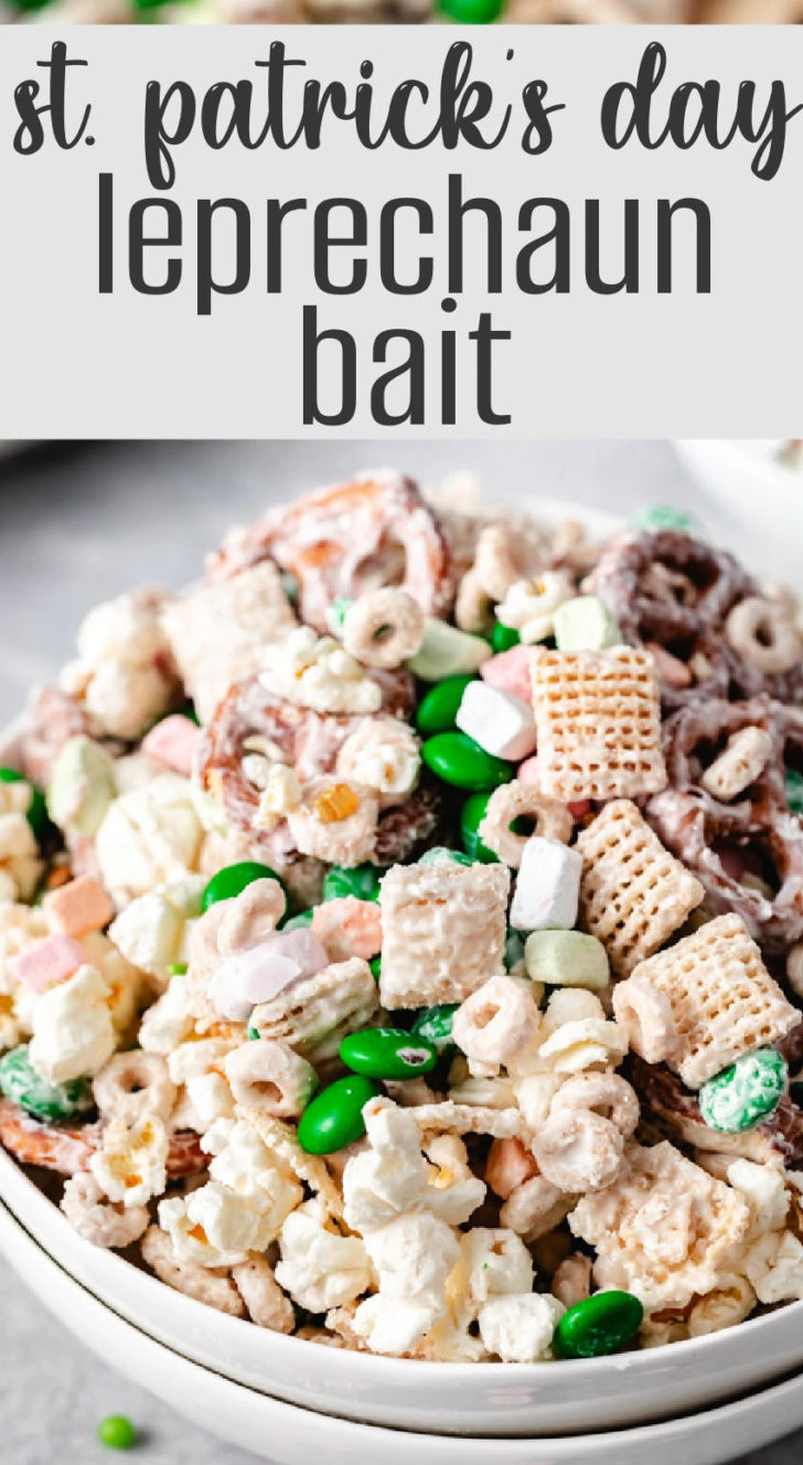 A close-up of a bowl filled with a crunchy snack mix of cereal, popcorn, pretzels, and green m&ms.